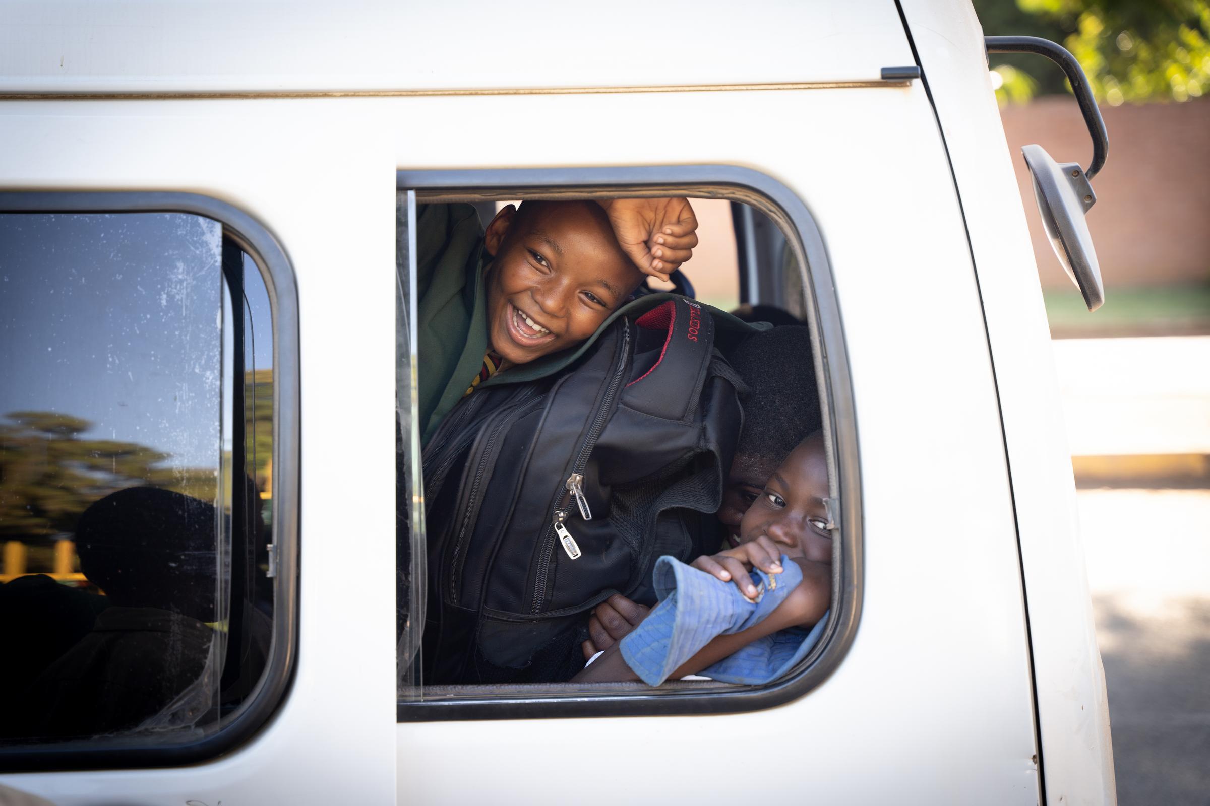 Zwei Kinder schauen lachend aus dem Fenster des Schulbusses, der sie sicher zur Schule bringt (Foto: Christian Nusch)