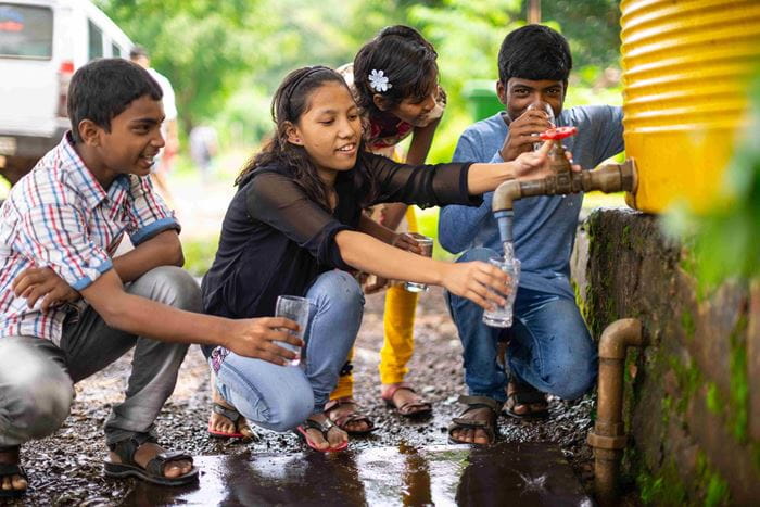 Vier Jugendliche aus Indien füllen lachend sauberes Wasser aus einem Brunnen in Gläser. (Quelle: Jakob Studnar) Vier Jugendliche aus Indien füllen lachend sauberes Wasser aus einem Brunnen in Gläser. (Quelle: Jakob Studnar)